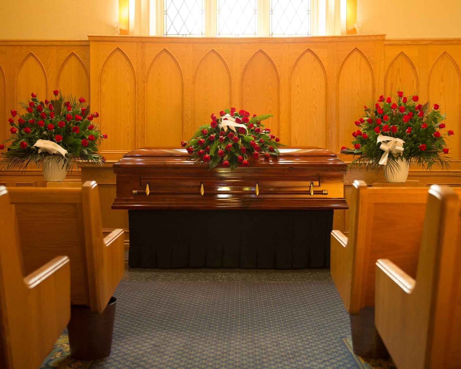 A wooden casket with red roses in a chapel, shown as an example of a traditional funeral setting.