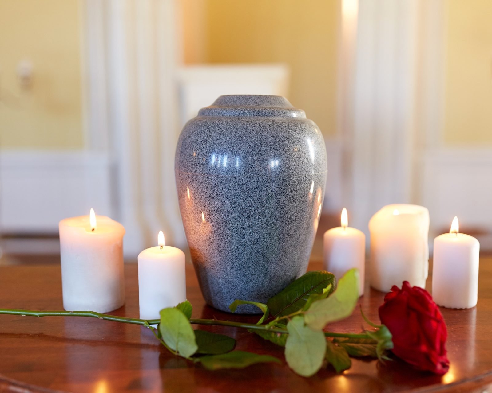 A cremation urn with candles and a rose on a wooden table.