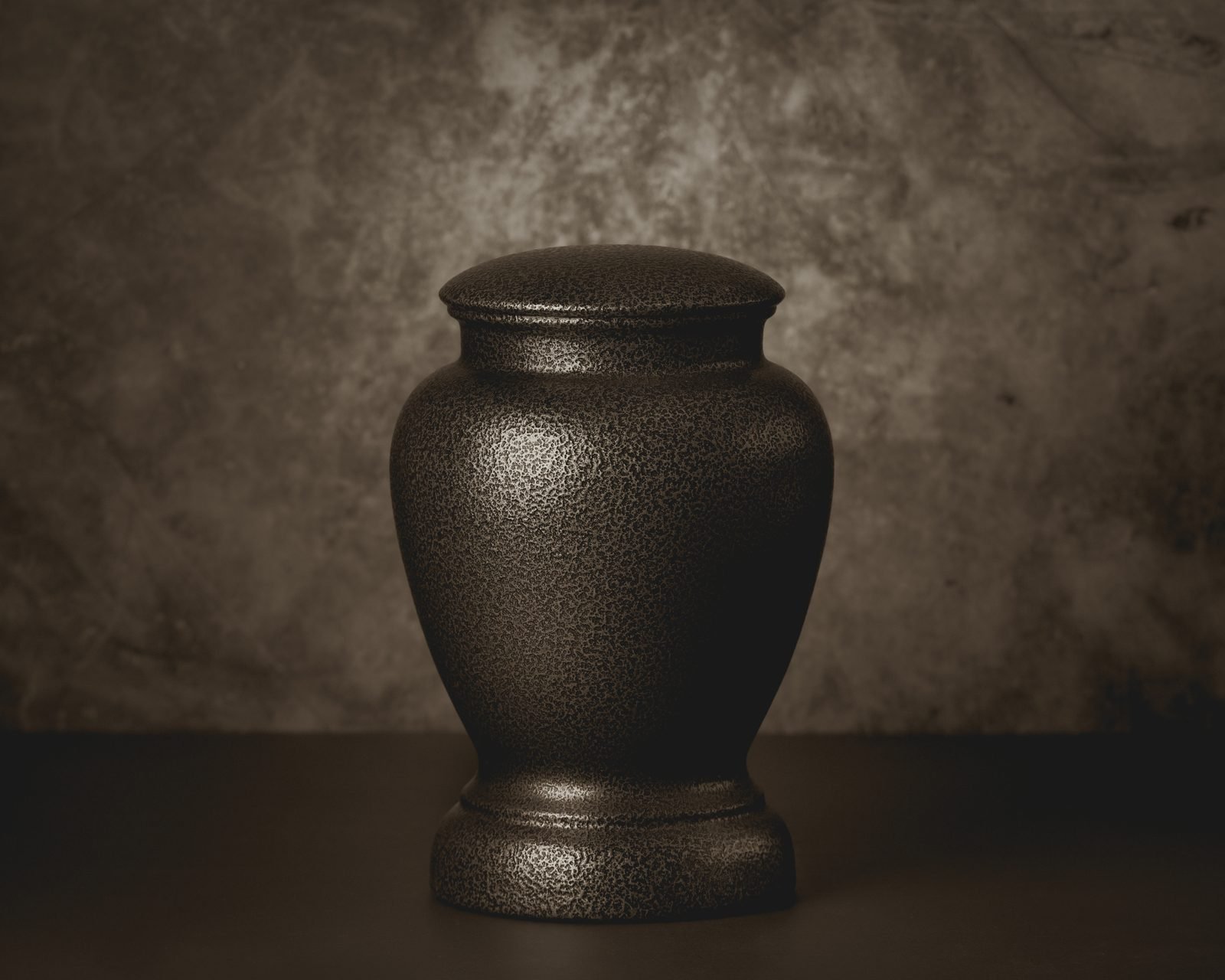 A dark cremation urn against a stone background.